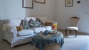 Un salon avec un canapé blanc, un plaid bleu, un plateau avec une théière et un fauteuil.