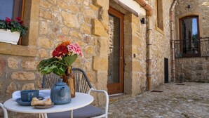 Un bâtiment en pierre avec une cour pavée, une table avec une chaise et un vase rempli de fleurs.
