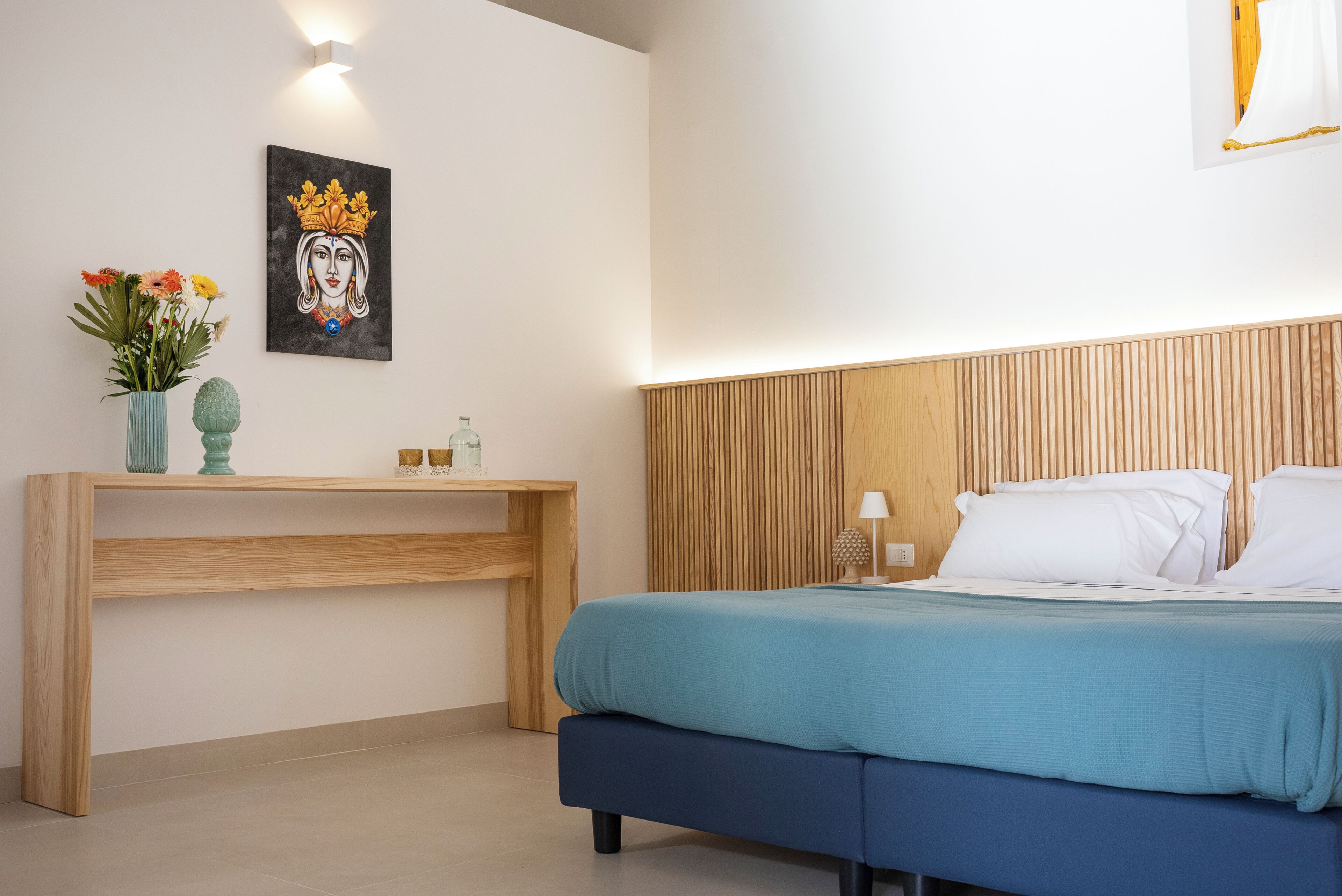Een slaapkamer met een houten hoofdbord, een bed met wit beddengoed, een nachtkastje met een lamp en een kunstwerk aan de muur.