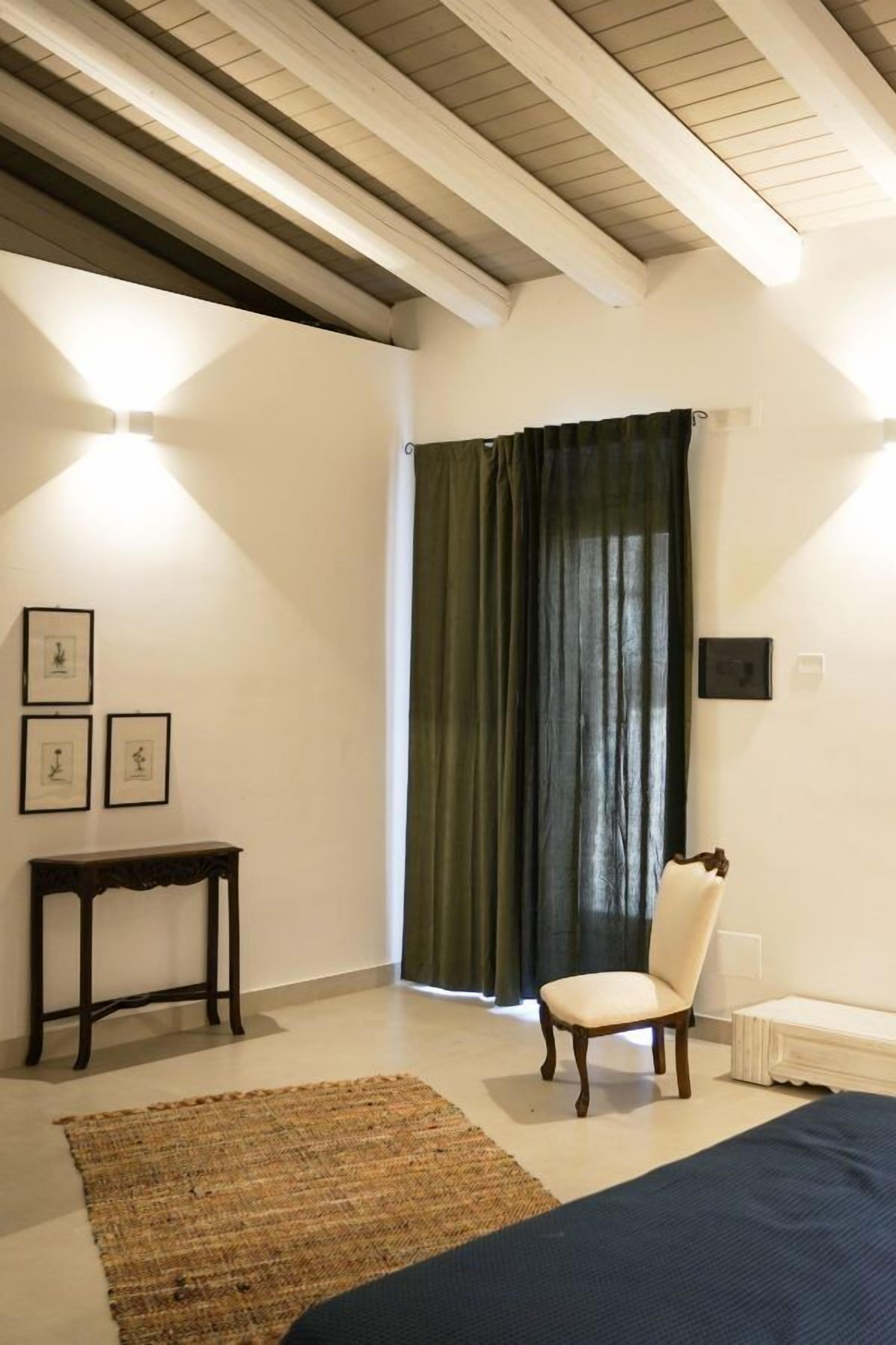 Ein Schlafzimmer mit einem Bett, einem Sessel, einem kleinen Tisch und einem Fenster mit Vorhängen.
