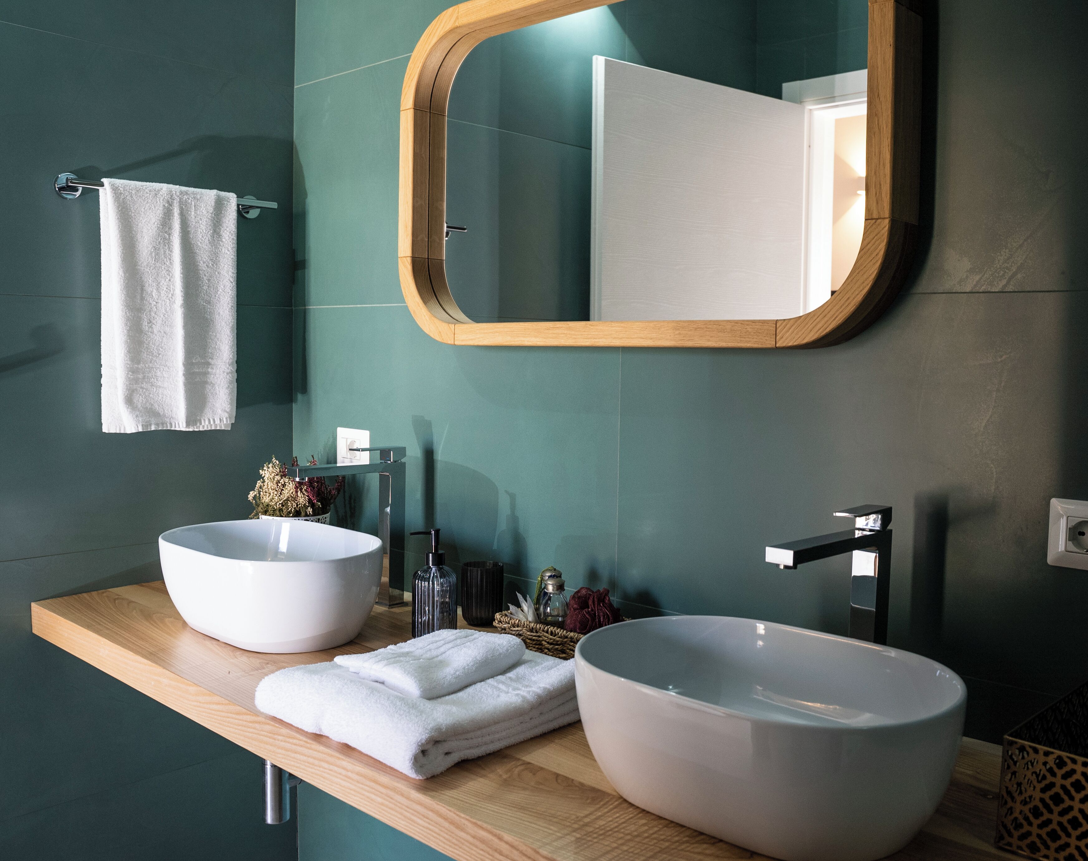 Een moderne badkamer met twee grote witte wasbakken, een houten aanrechtblad, een spiegel met houten lijst en een handdoek aan de muur.