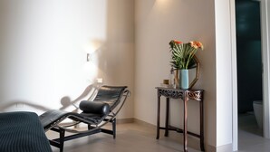 Un espace d’attente moderne, comprenant un fauteuil confortable, une petite table ornée d’un vase de fleurs et un luminaire fixé au mur.