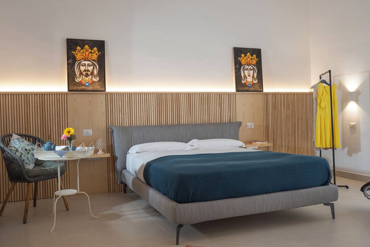 A modern bedroom with a bed, a chair, a table with a vase of flowers, and two wall-mounted paintings.