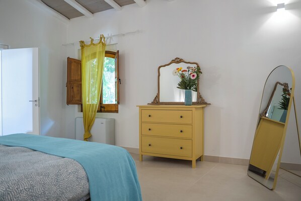 Une chambre à coucher avec un lit, une commode, un miroir et une fenêtre avec des rideaux.