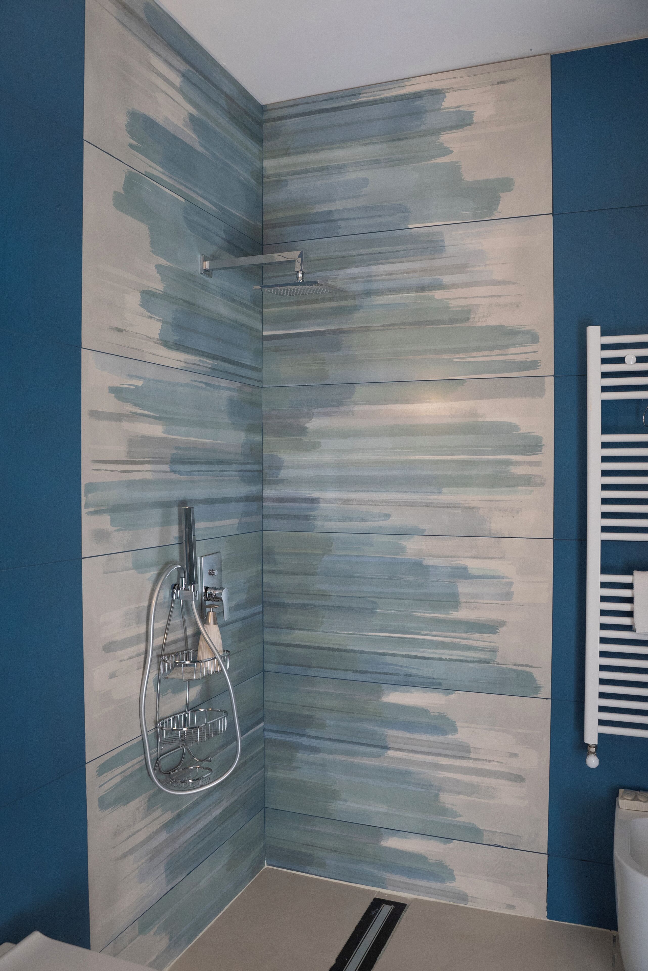 Un área de ducha con diseño moderno, un cabezal de ducha metálico y un perchero blanco.