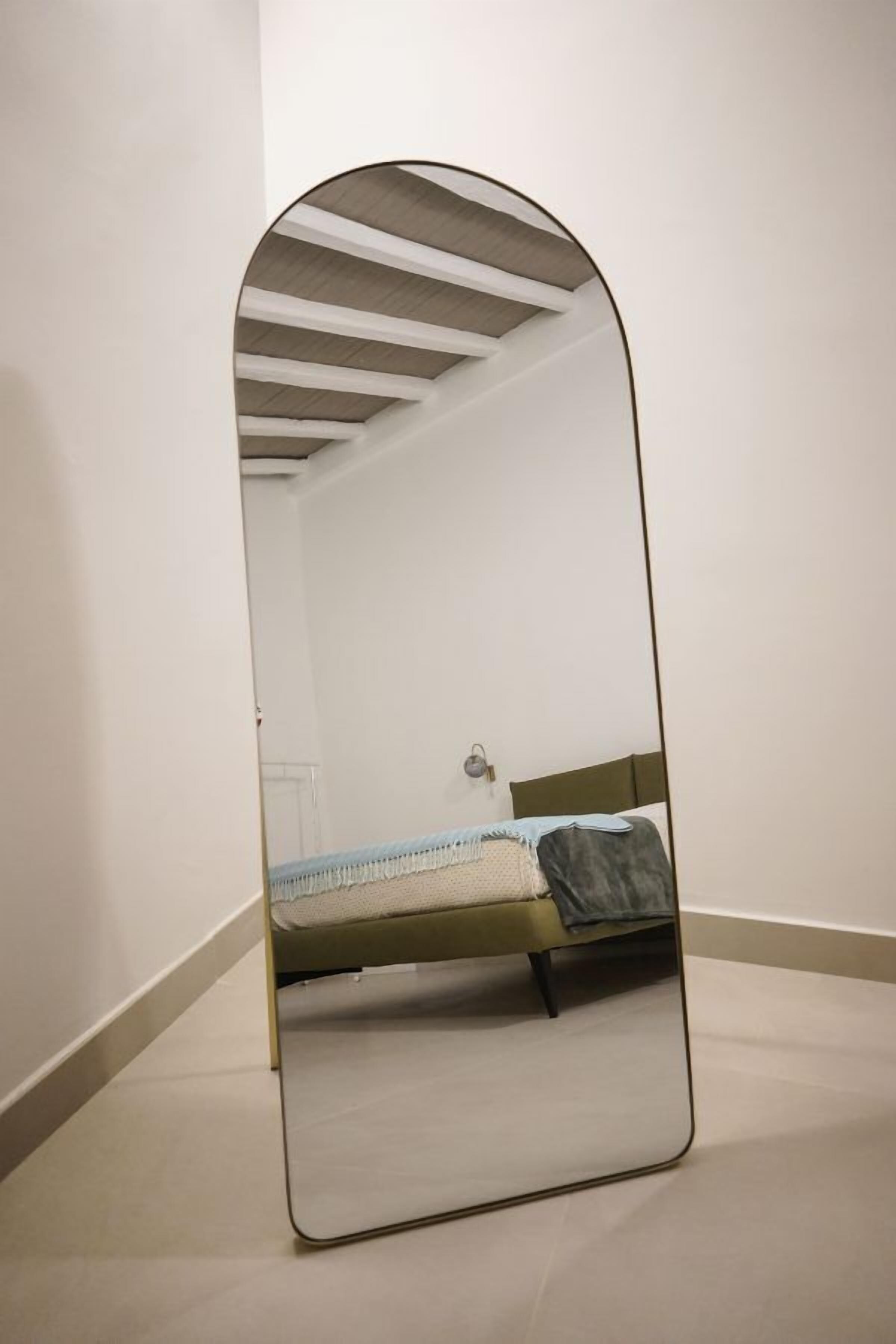 A room with a bed, a mirror, and a ceiling with wooden beams.