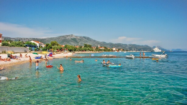 A coastal beach scene with clear turquoise water, people swimming and sunbathing, and boats docked near the shore. - Charming Studio Apartment Near the Sea (Orebic)
