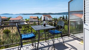 A balcony with a table and chairs, overlooking a body of water and houses. - Charming Studio Apartment Near the Sea (Orebic)