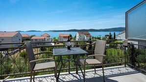 Un balcon avec des fauteuils en osier et une table, d’où l’on a vue sur un lac et des maisons.