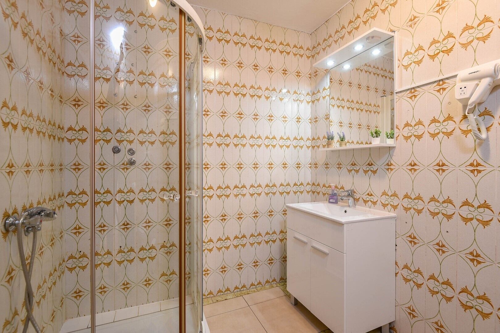 Ein Badezimmer mit gestreiftem Wandpapier, einer Duschkabine aus Glas, einem weißen Waschbecken und einem Haartrockner auf einem Regal.