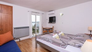 A bedroom with a bed, a TV, a chair, a table, a radiator, and a view of the outdoors. - Charming holiday studio apartment (Orebic)