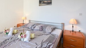 A neatly made bed with floral arrangements, a bedside table with a lamp, and a painting on the wall. - Charming holiday studio apartment (Orebic)