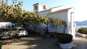 Un edificio residencial con entrada pavimentada, coches aparcados y vista al mar.