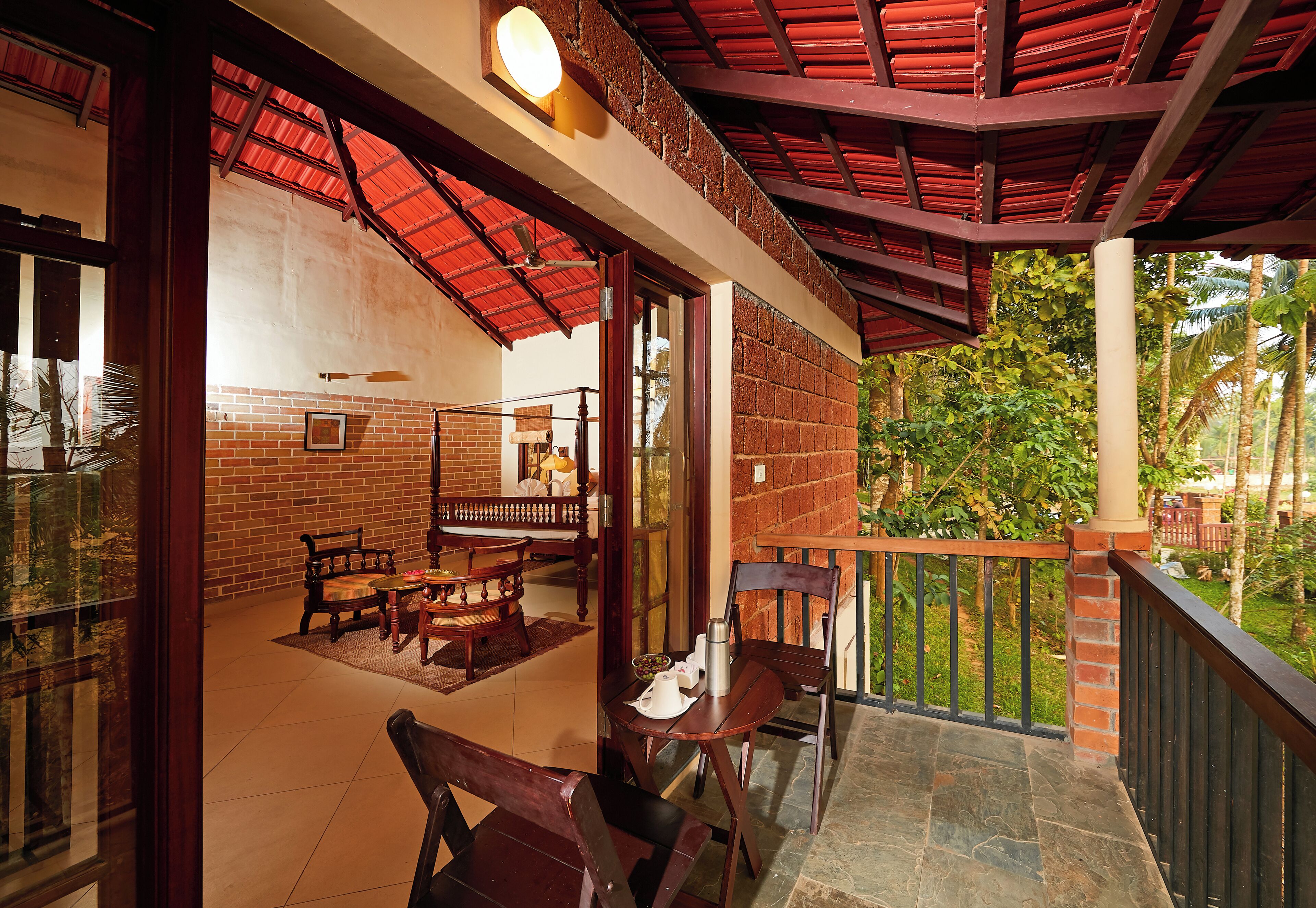 A covered outdoor seating area with brick walls, wooden furniture, and a view of greenery.