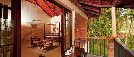 A covered outdoor seating area with brick walls, wooden furniture, and a view of greenery.