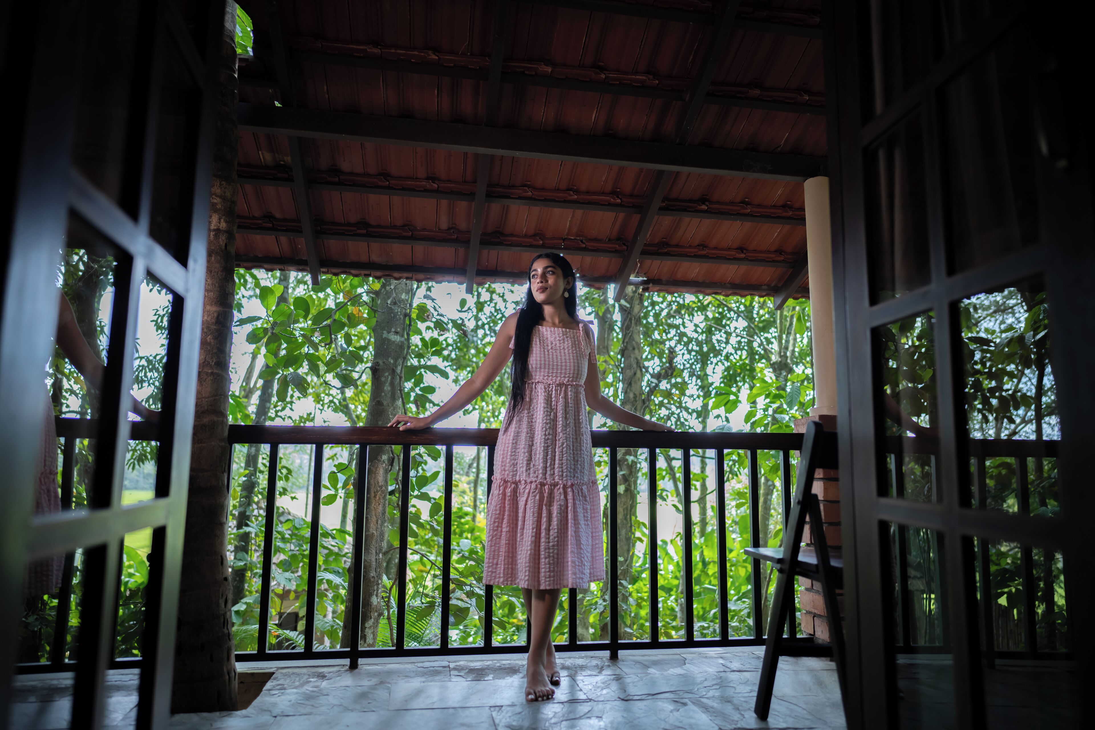 A woman standing on a balcony with a view of lush greenery.