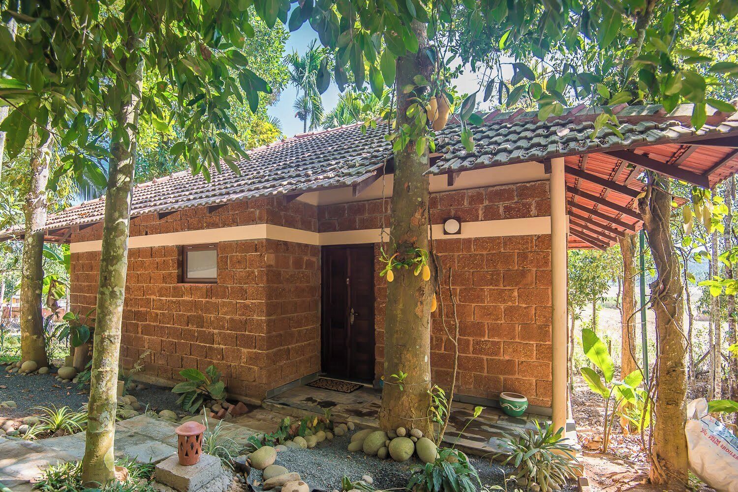 A small brick building with a tiled roof, surrounded by trees and plants.
