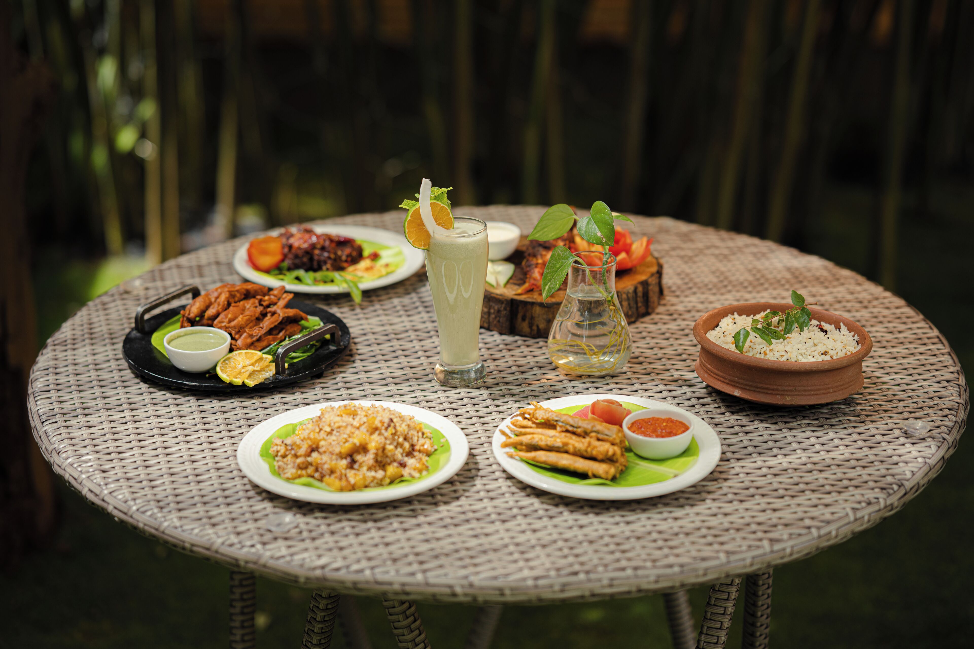A round wicker table with various dishes including rice, fried items, and a drink.