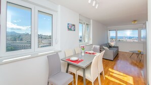 Ein moderner Essbereich mit Tisch für zwei Personen, großen Fenstern mit Blick auf die Stadt und einer gemütlichen Sitzecke mit einer Couch.