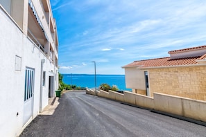 A narrow street with a building on the left and a view of the sea on the right.