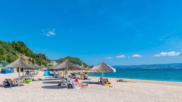 A beach with thatched umbrellas and sun loungers, a clear sky, and calm sea.