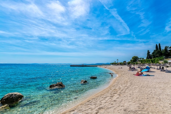 Une plage avec une eau claire, des rochers et des parasols.