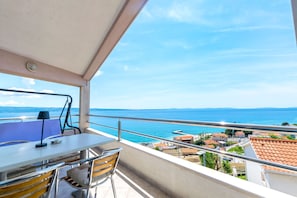 Un balcon avec une table, des chaises et une vue sur la mer et la ville.