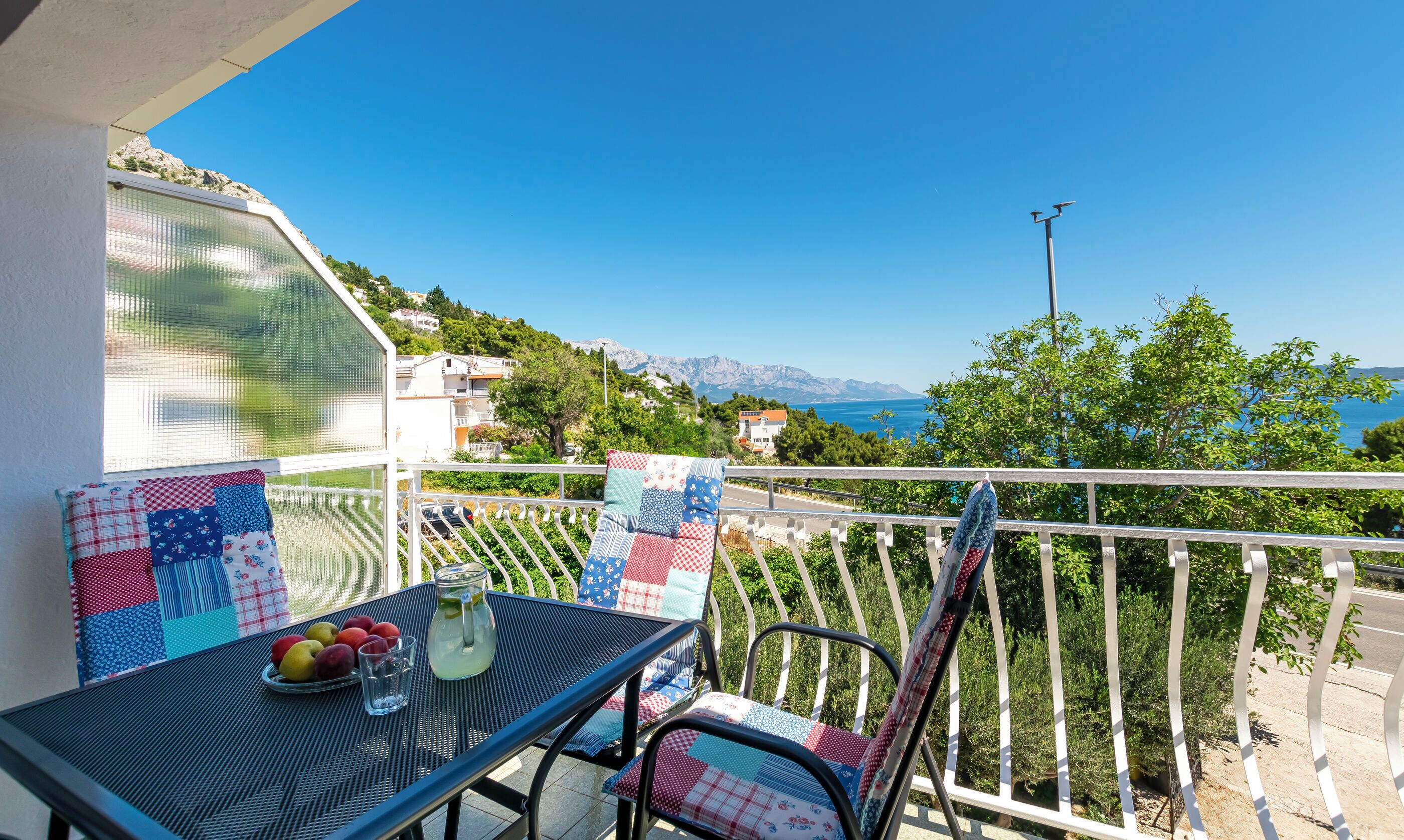 Uma varanda com mesa, cadeiras e vista para o mar e montanhas.