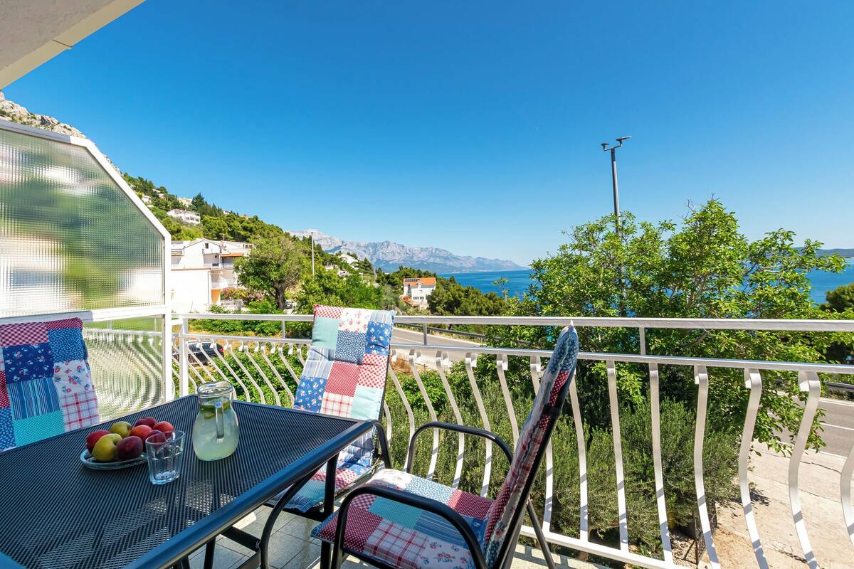 A balcony with a table, chairs, and a view of the sea and mountains.