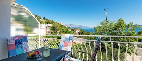 A balcony with a table, chairs, and a view of the sea and mountains.