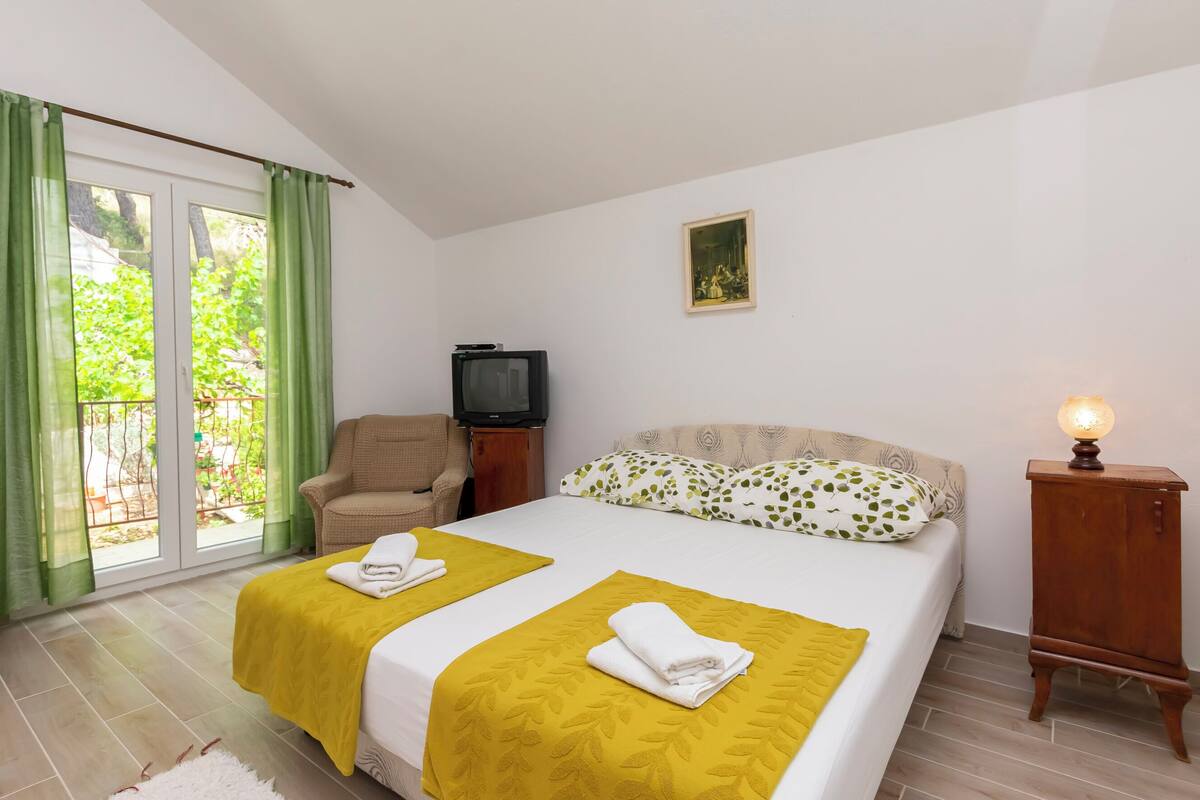 A bedroom with two beds, a chair, a television, and a nightstand with a lamp.