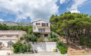 A two-story building with a balcony, surrounded by trees and a mountainous backdrop. - Apartments Andi (Omis)