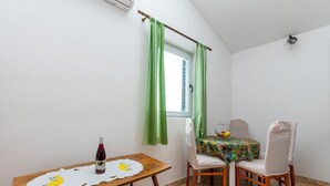 Un petit coin repas avec une table, des chaises, une fenêtre avec des rideaux et une bouteille de vin.