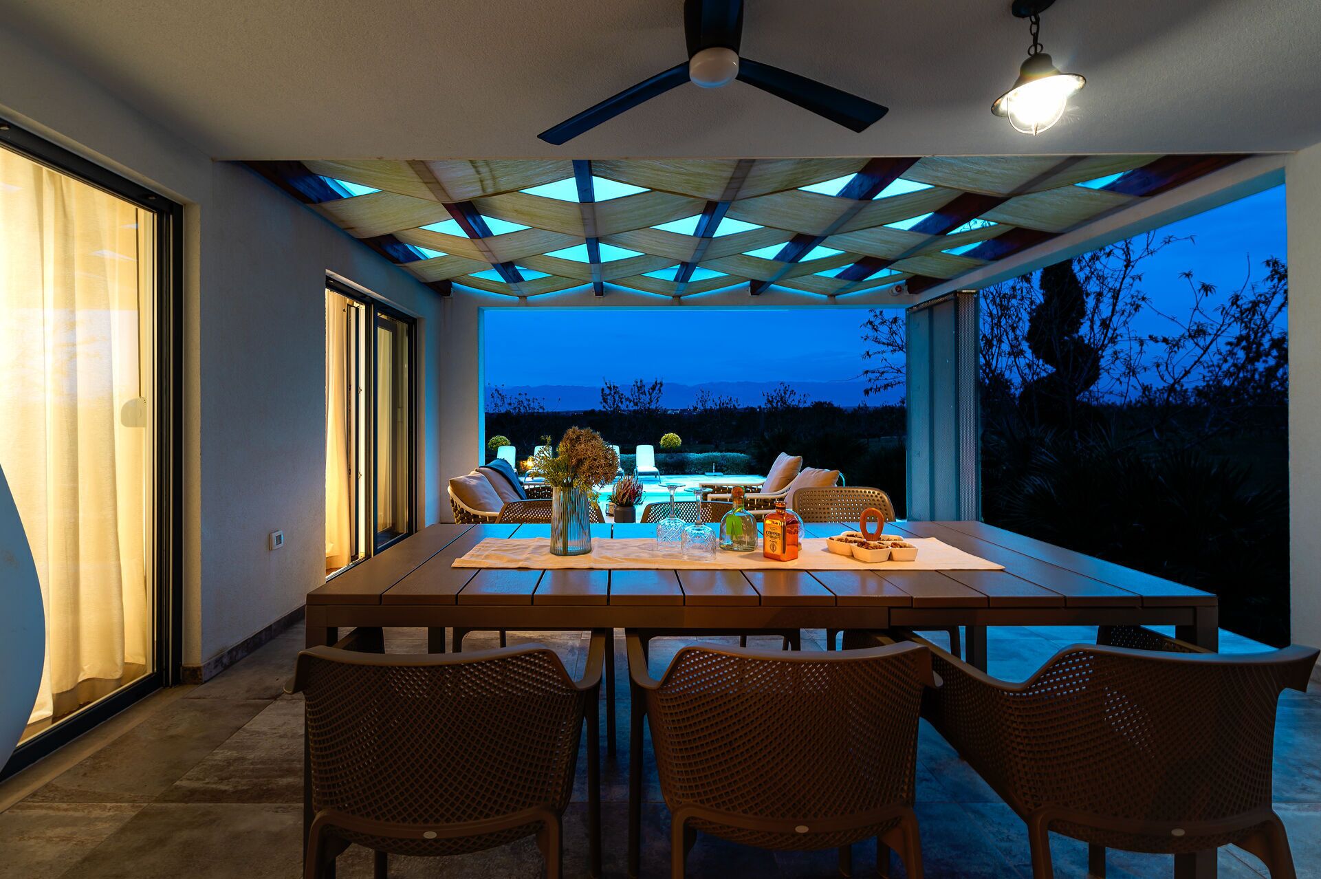 A dining area with a table set for four, surrounded by wicker chairs, under a ceiling with a geometric pattern.