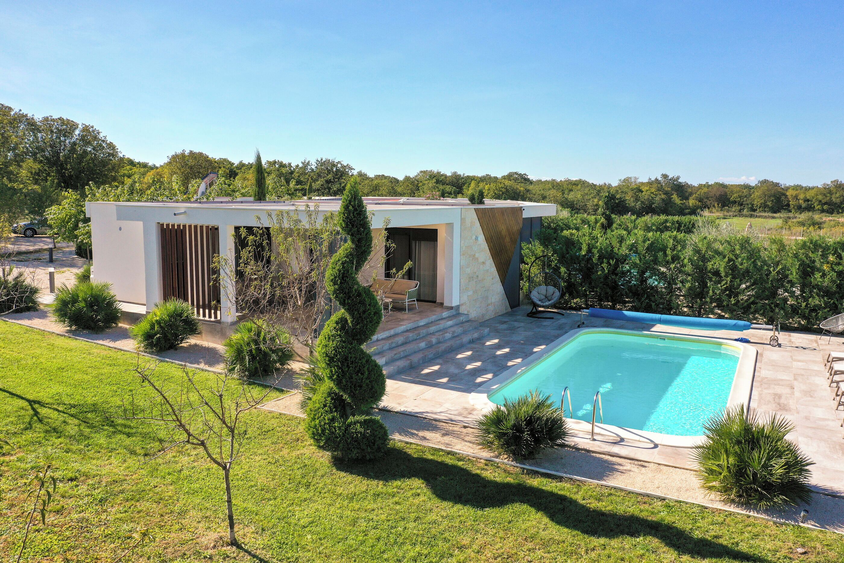 Une maison moderne dotée d’une piscine, entourée de pelouses et d’arbres bien entretenus.