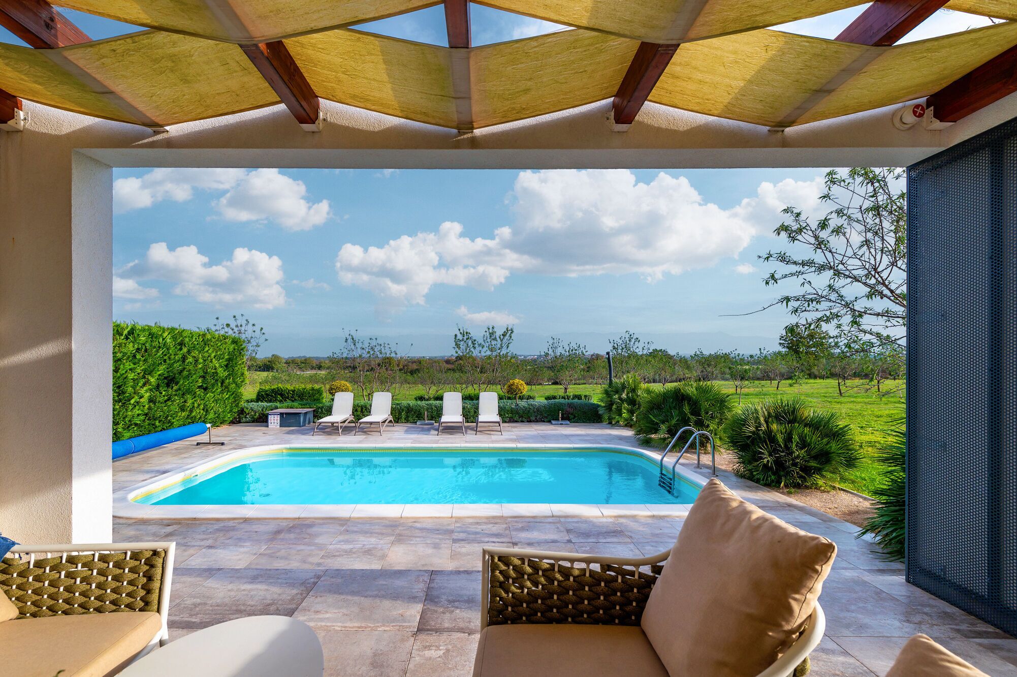 Un espacio al aire libre techado con piscina, sillas de descanso y vistas a un paisaje verde.
