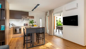A modern kitchen with a dining area, a TV mounted on the wall, and a sliding glass door leading to a balcony. - Villa Royal Green Two (Nin)