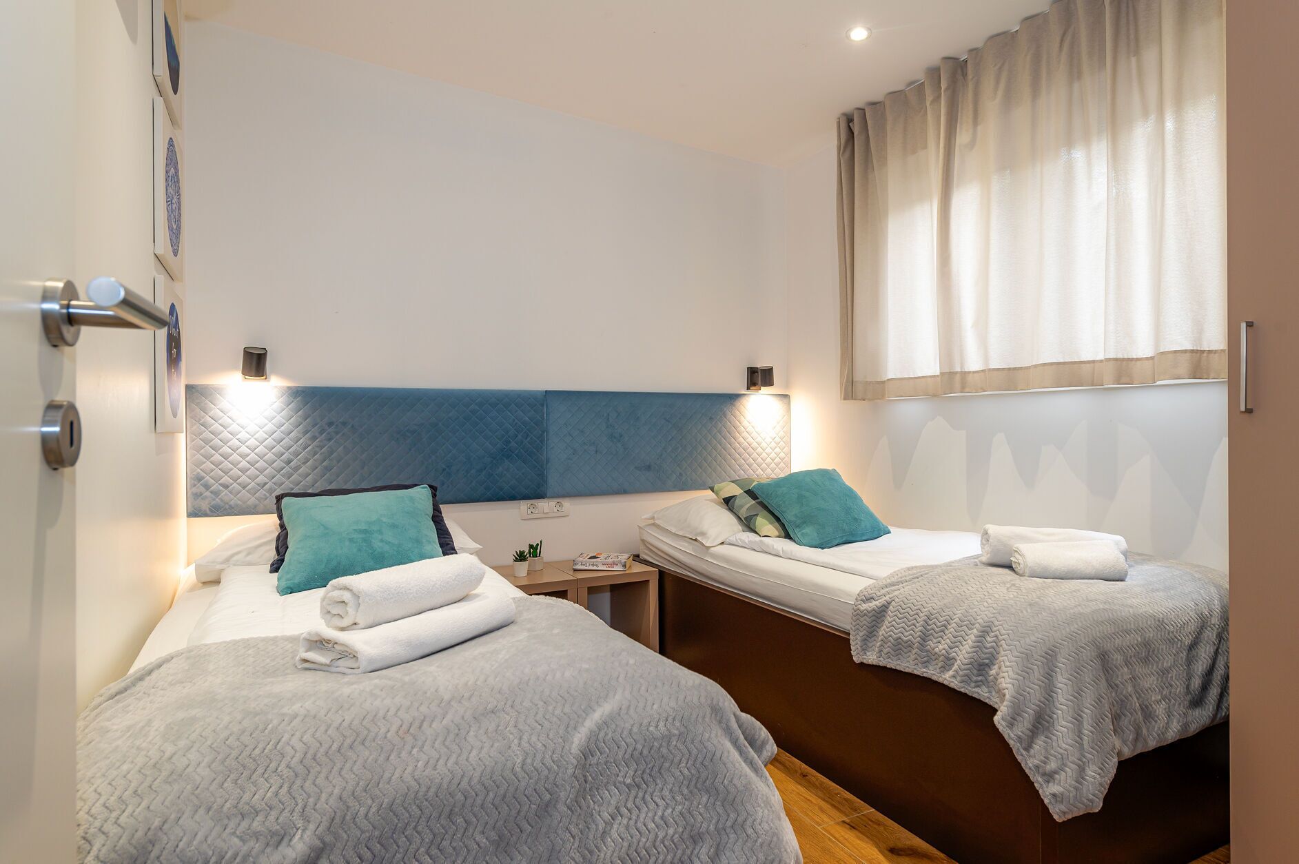 A hotel room with two beds, each with a headboard, bedside tables, and lamps.
