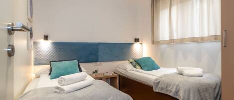 A hotel room with two beds, each with a headboard, bedside tables, and lamps.