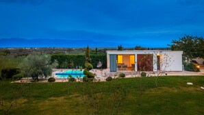 A modern house with a pool, surrounded by greenery and mountains in the background.