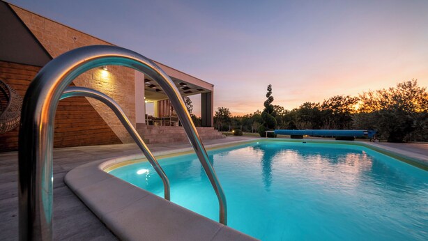 A modern outdoor pool with a metal ladder, surrounded by a wooden deck and a covered seating area.