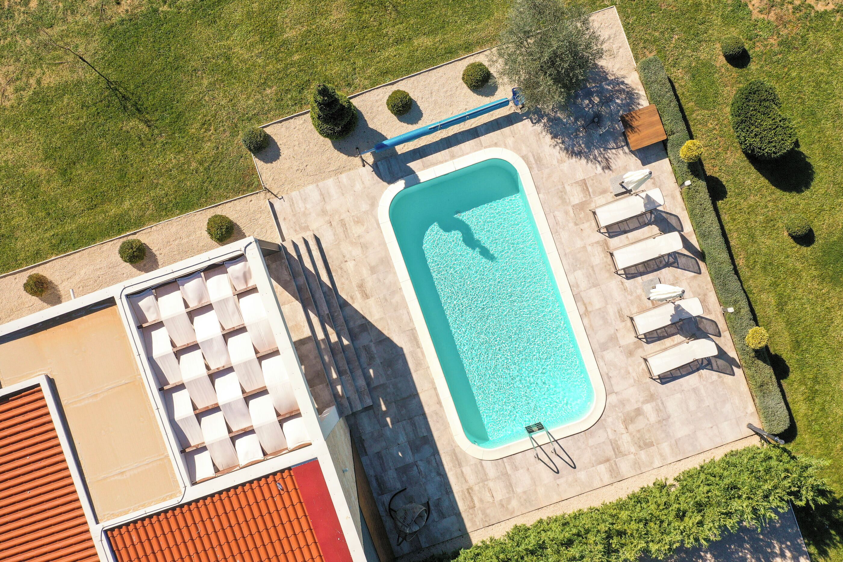 An aerial view of a residential property with a swimming pool, a covered patio area with lounge chairs, and a well-maintained lawn.