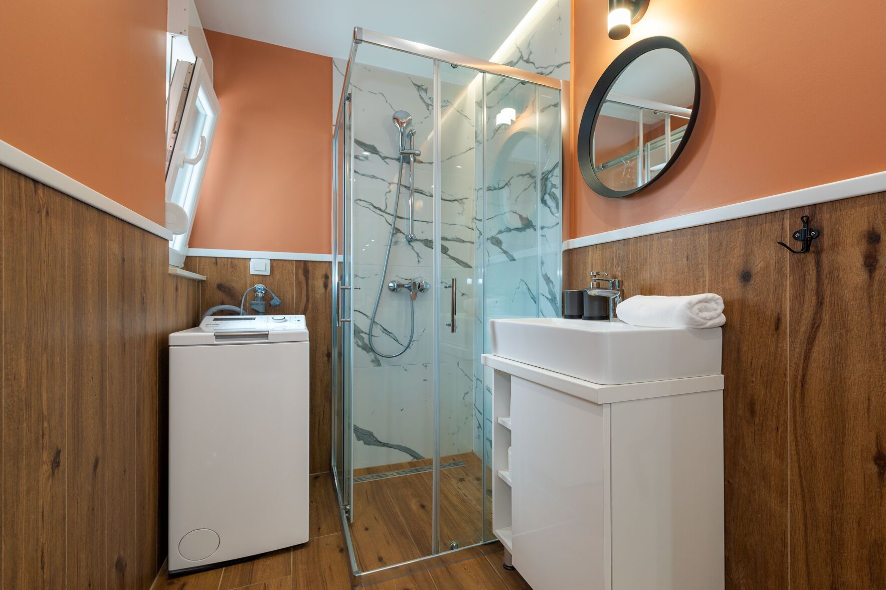 A bathroom with a glass shower enclosure, a white sink, and a wooden panel wall.