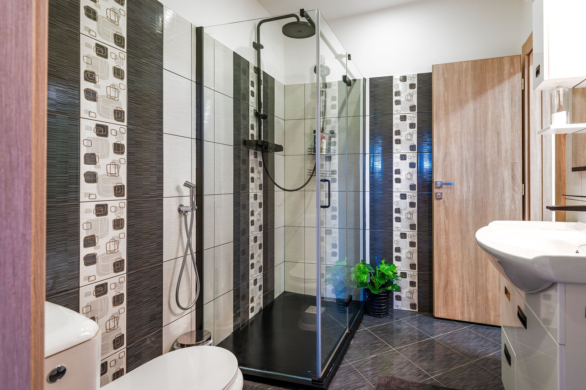 A modern bathroom with a glass-enclosed shower, a white sink, and a wooden door.