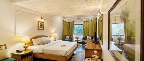 A hotel room with a bed, bedside tables, a desk, a chair, a small table with a lamp, a window with curtains, and a framed picture on the wall.