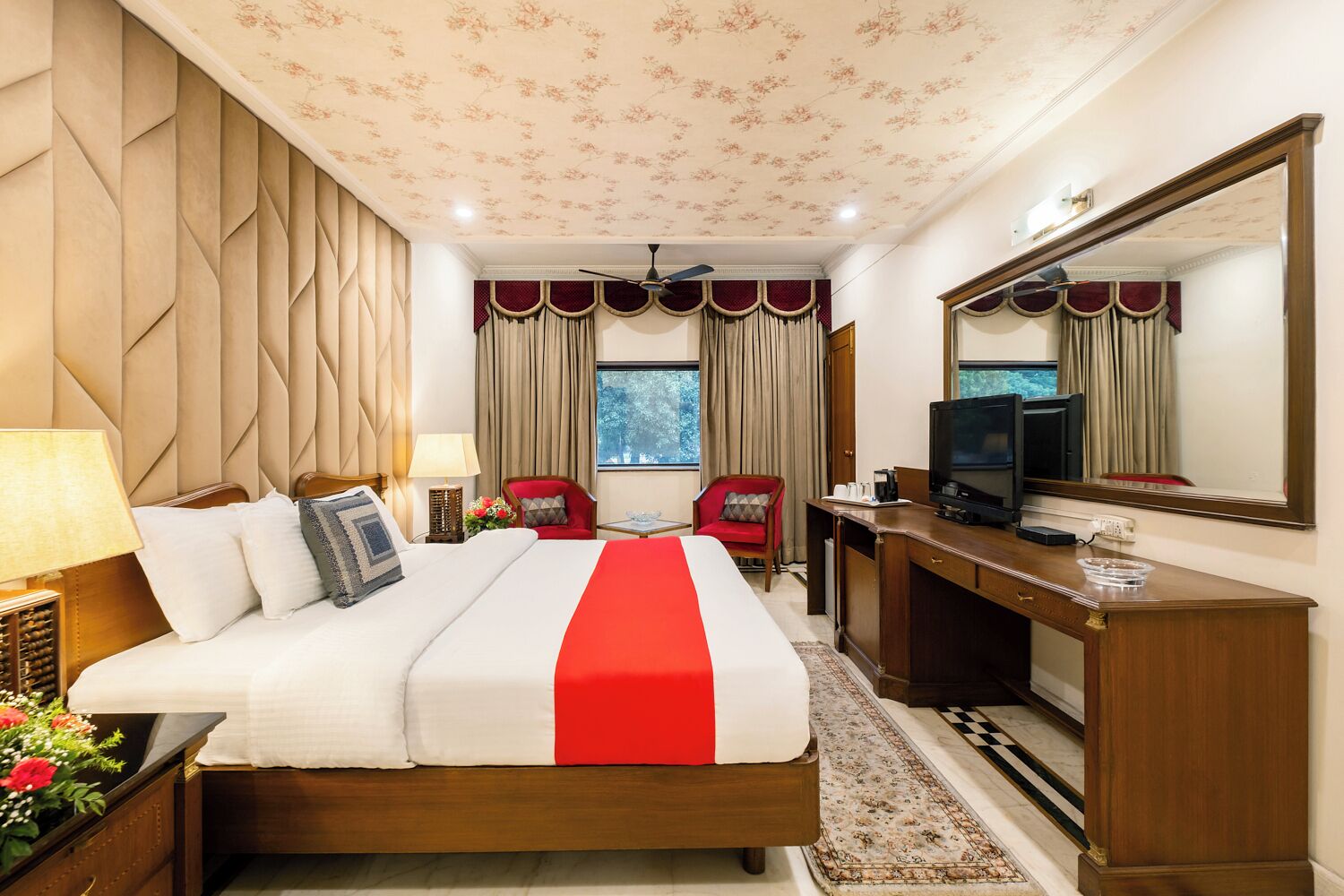A hotel room with a large bed, a desk, a television, and a mirror.
