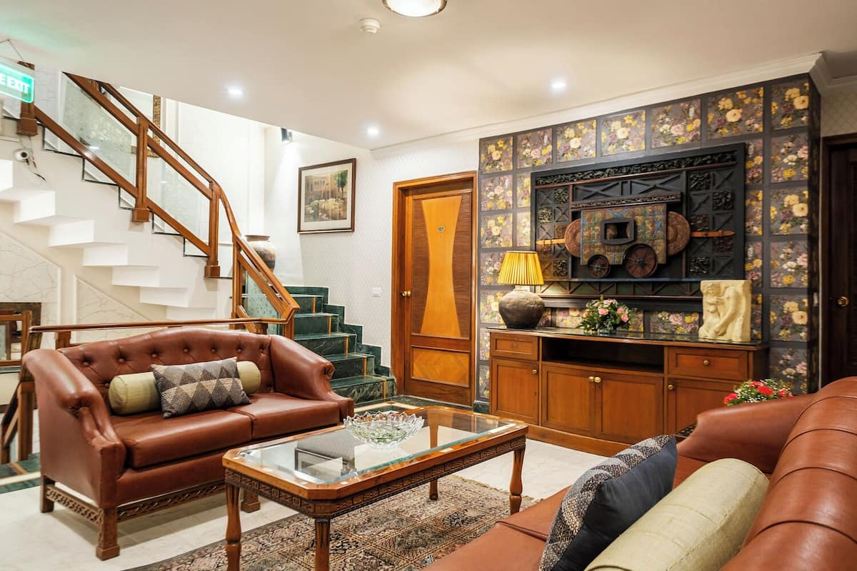 A spacious living room with a leather sofa, a glass coffee table, and a staircase leading to an upper floor.