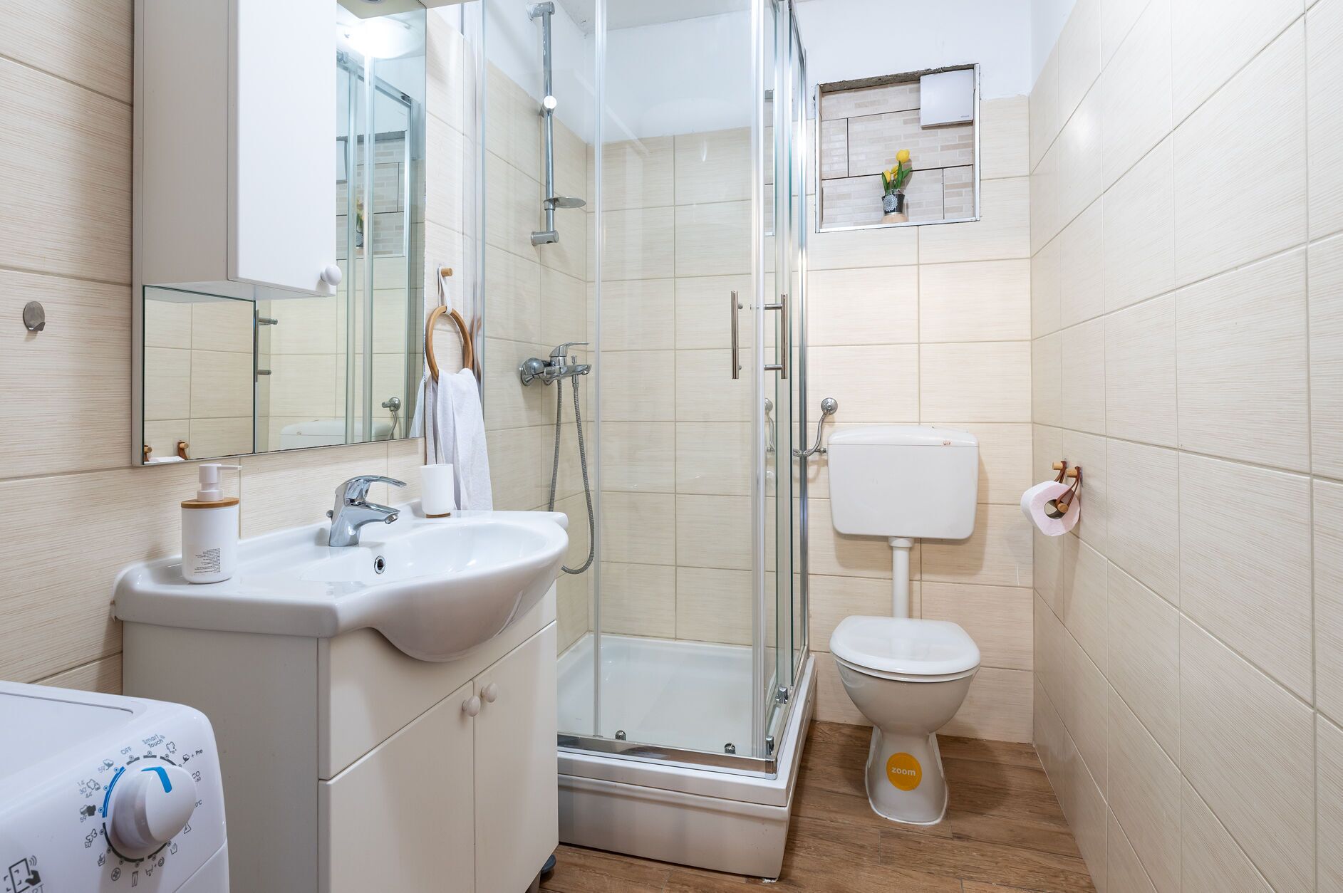 A modern bathroom with a glass shower enclosure, a white sink with a soap dispenser, a toilet, and a mirror above the sink.