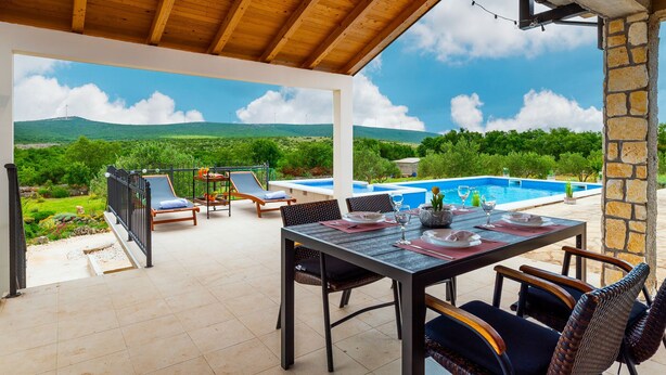 A covered outdoor area with a pool, lounge chairs, and a dining table set for four. - Villa Kiara (Unesic)