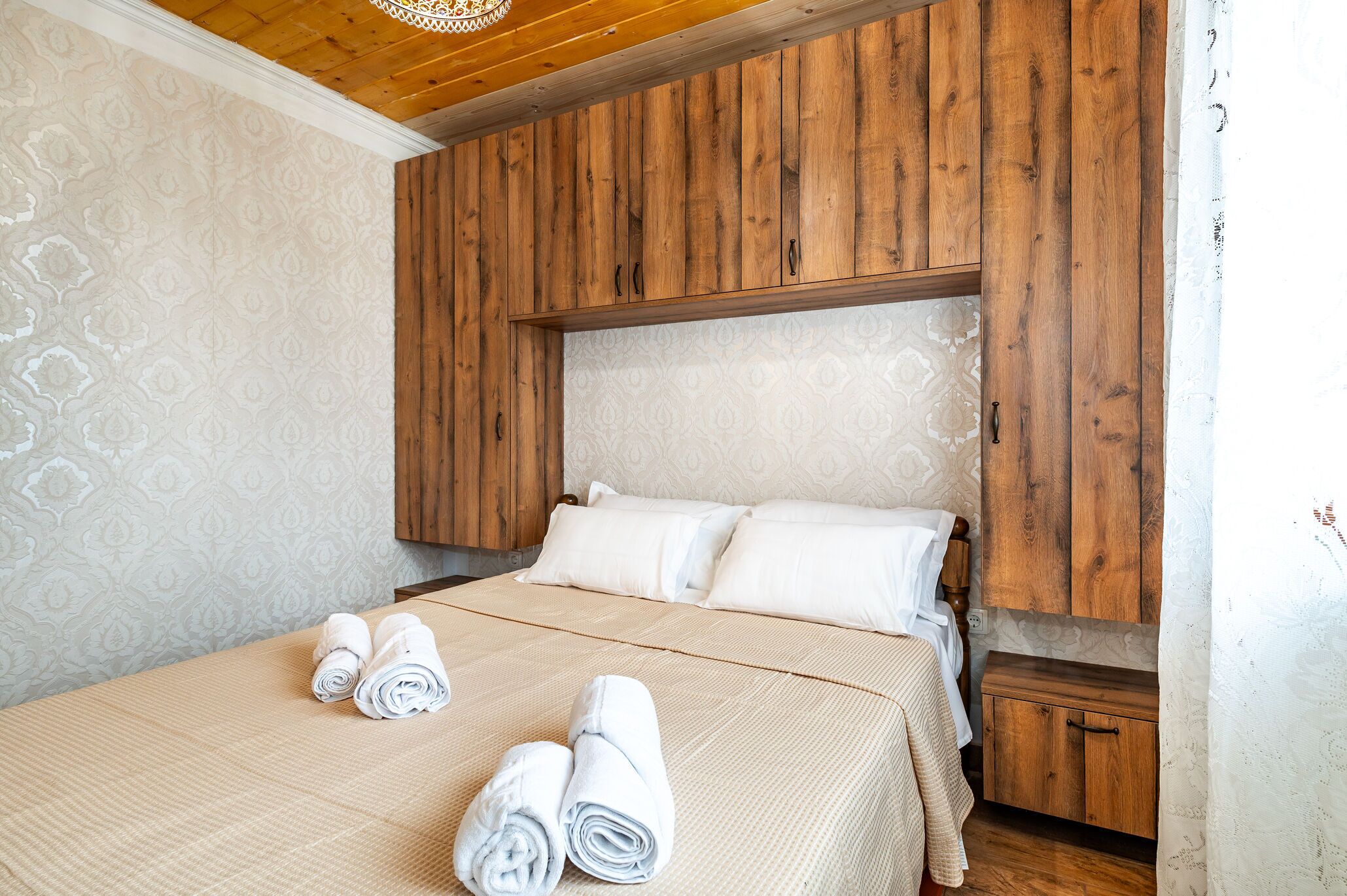 A neatly made bed with rolled towels, wooden paneling on the wall, and a small wooden cabinet.